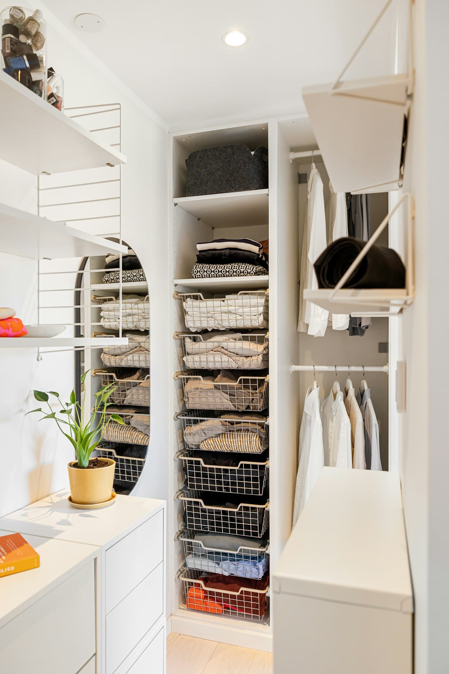 A white walk-in closet with garments hung in a row, folded items on shelves and baskets on the floor.